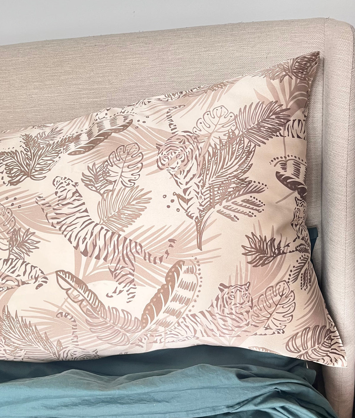Champagne gold tiger print pillowcase on a dark teal green bedspread and a headboard in the background.