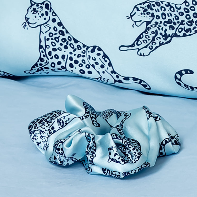 Close up of a MYRN light blue leopard print silk scrunchie.