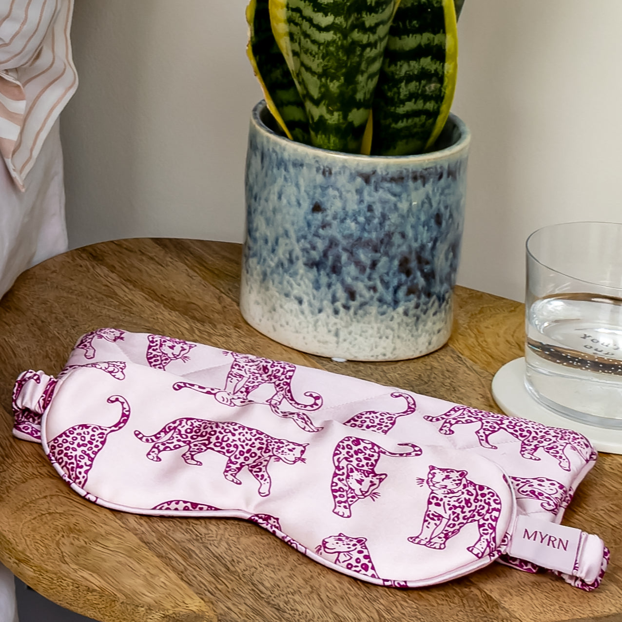 Pink leopard print silk eye mask and matching travel case on a bedside table.