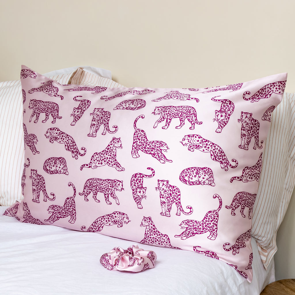 Pink leopard print silk pillowcase on a bed with a matching pink scrunchie