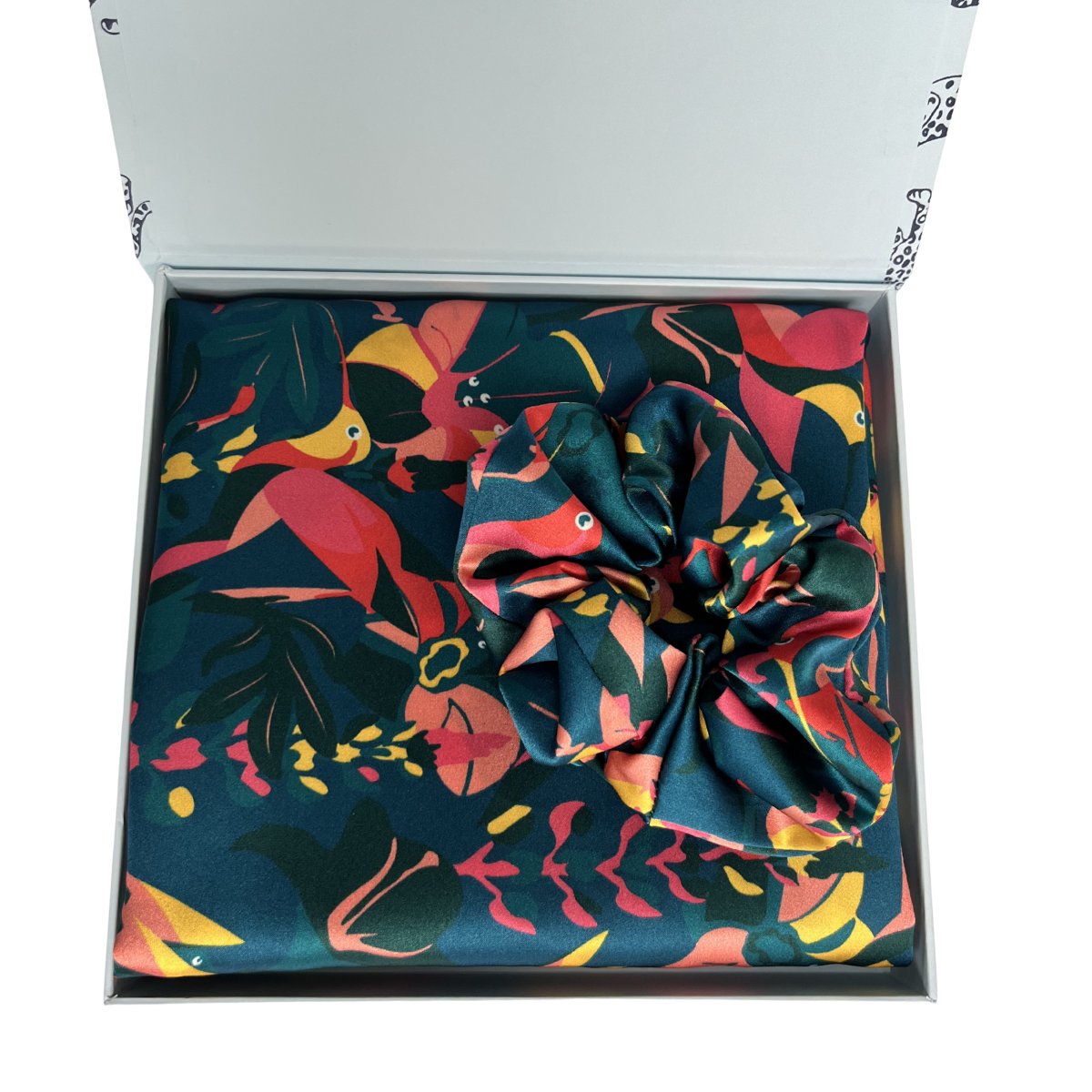MYRN Silk floral hummingbird print (green, pink, yellow) silk pillowcase folded, with a large silks scrunchie inside a presentation box on a white background.
