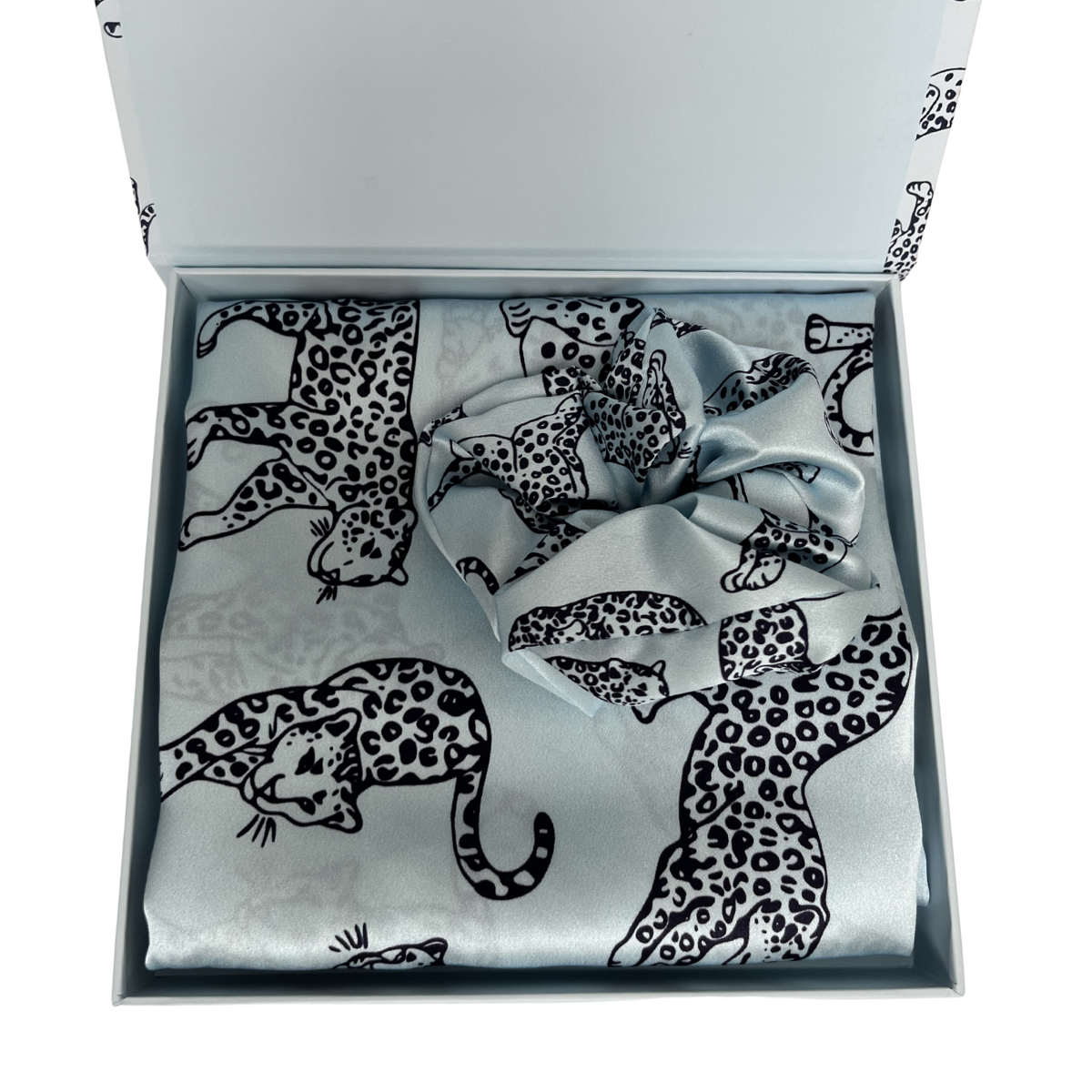 MYRN Silk light blue leopard print silk pillowcase folded with a matching silk scrunchie, inside a presentation box on a white background.