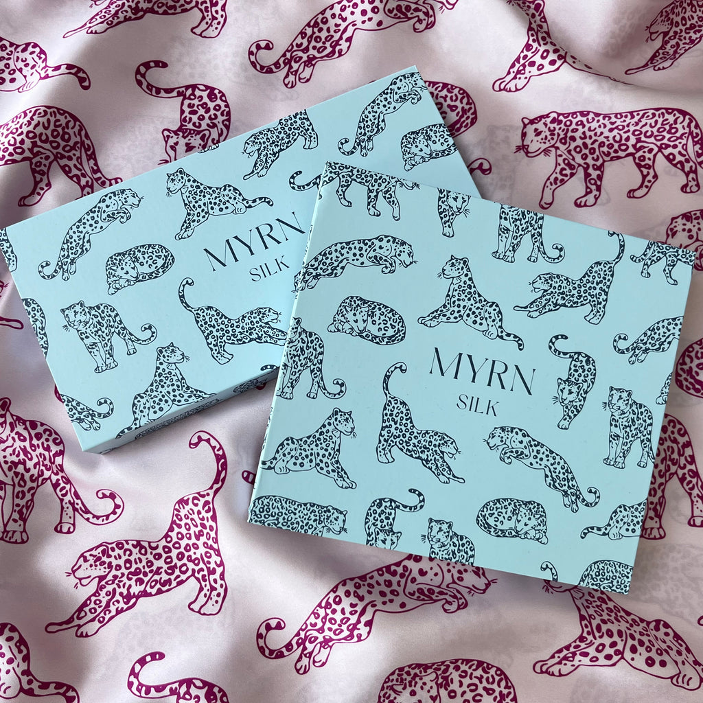 Image of 2 light blue leopard print MYRN Silk gift boxes laying on pink leopard print silk fabric.