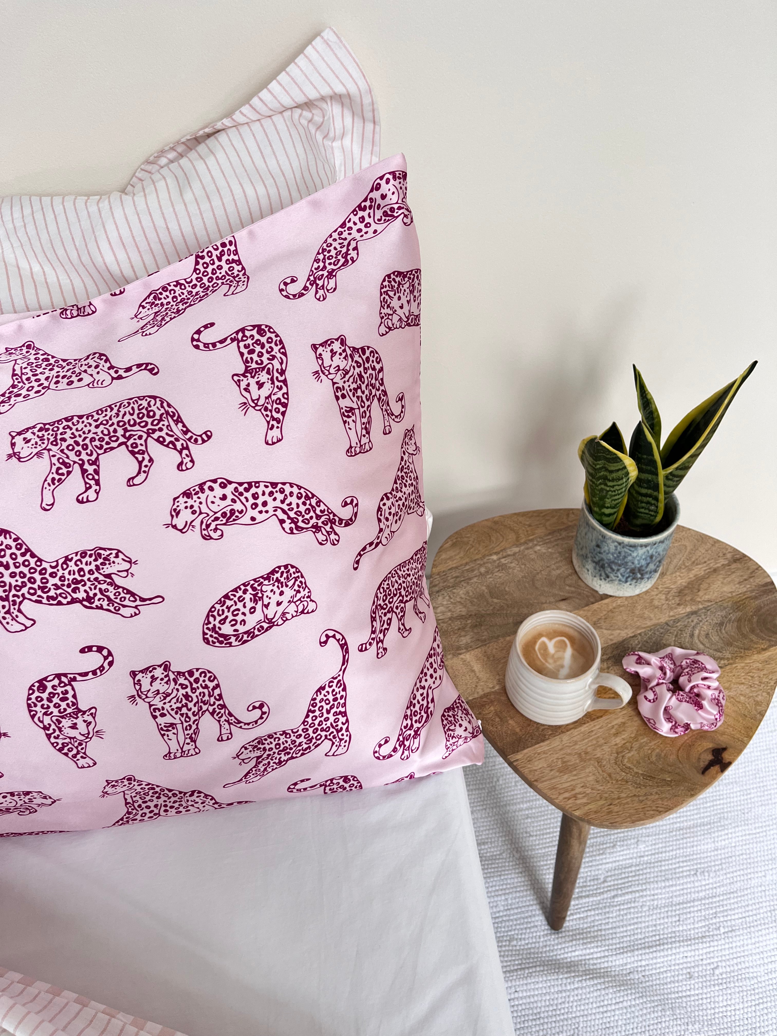MYRN Silk pink leopard print pillowcase on a bed with a pink silk scrunchie and a coffee cup with heart on the table